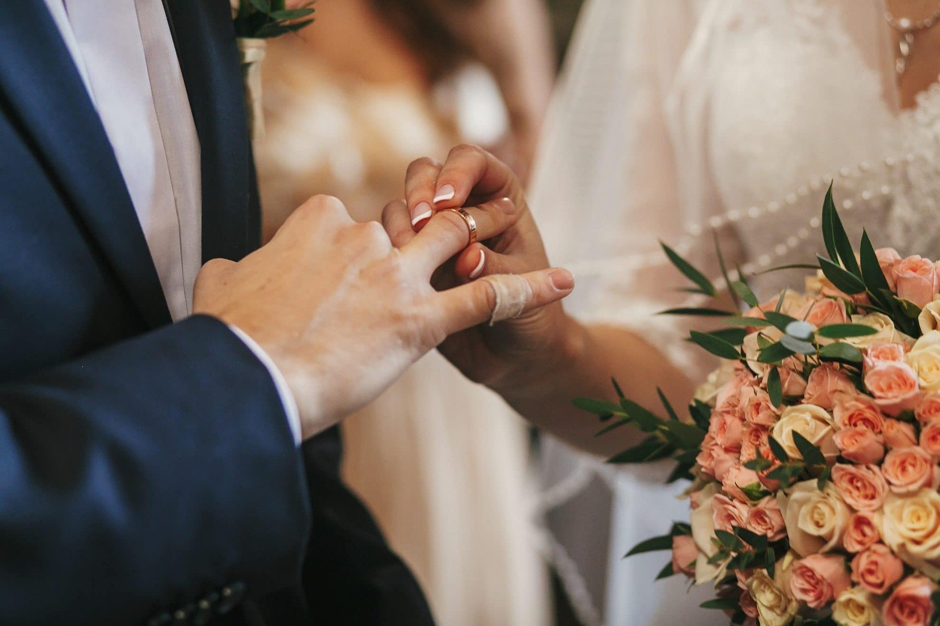 A bride places the wedding ring on her groom's finger.