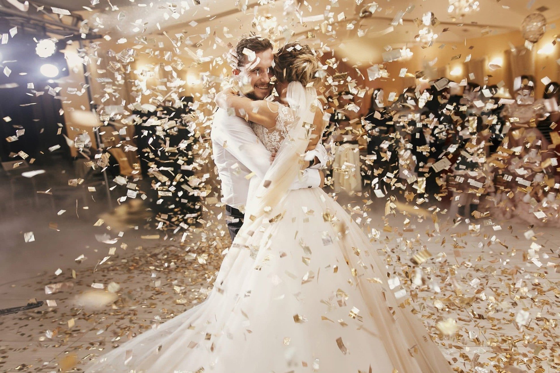 Bride and groom  hug during their first dance. Gold confetti falling from above.