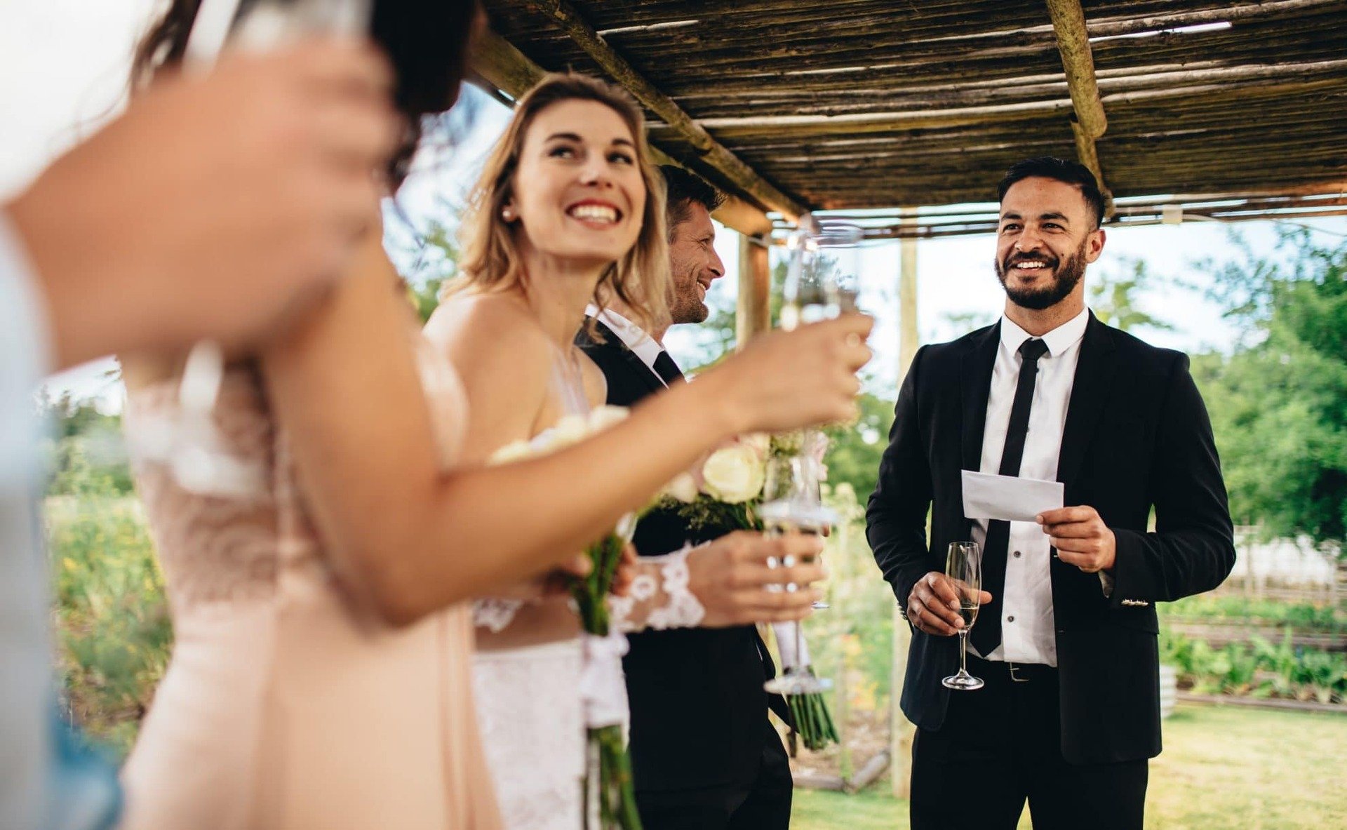 A best man stand in front of a small number of smiling guests.