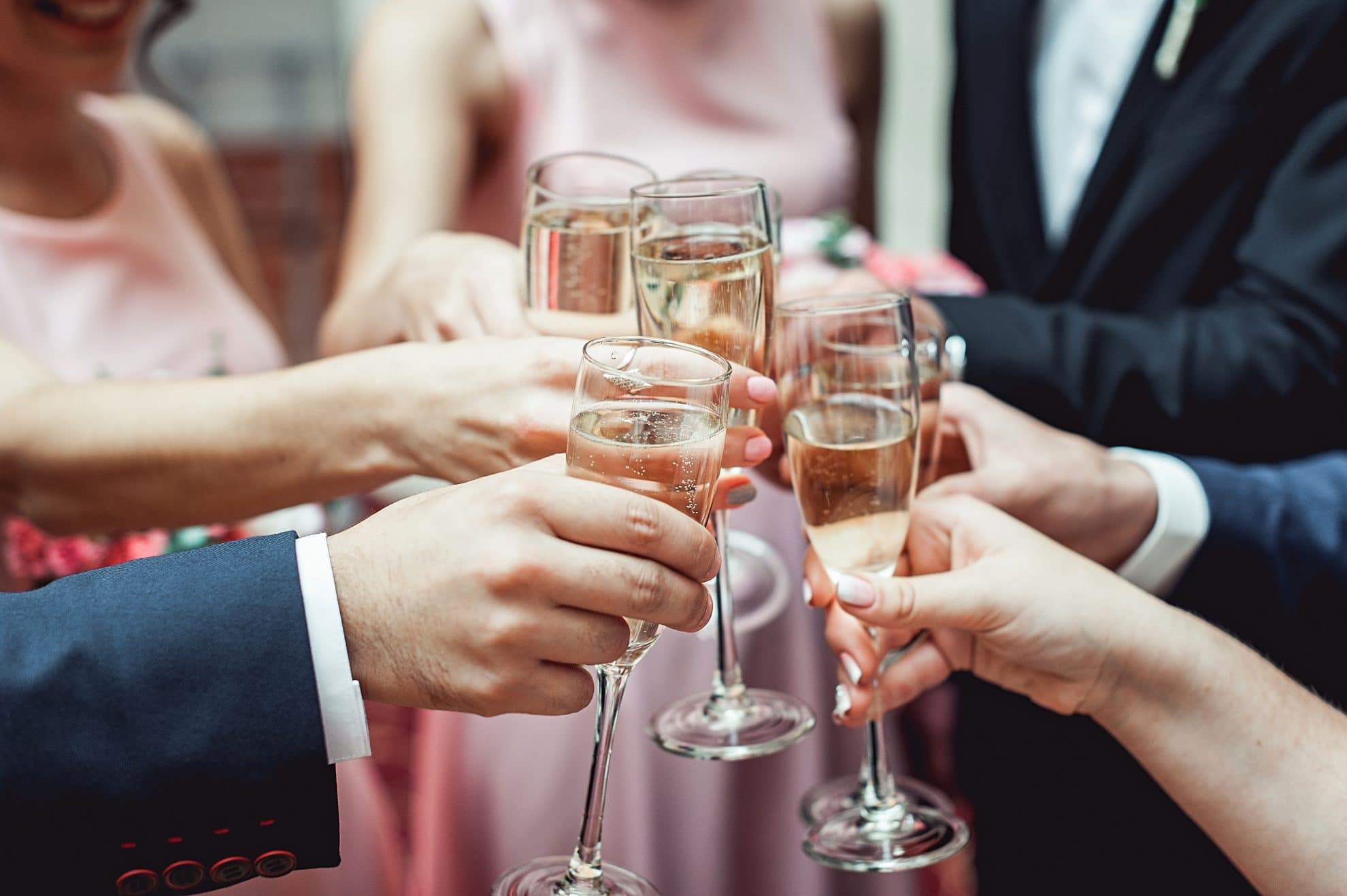 Champagne glasses are held together toasting. Image used in the How To Write The Perfect Best Man Speech and Nail It article.